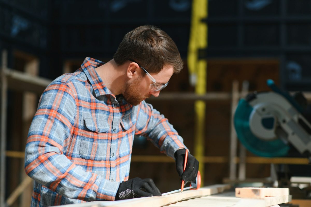 Professional carpenter in uniform cutting wooden board at sawmill